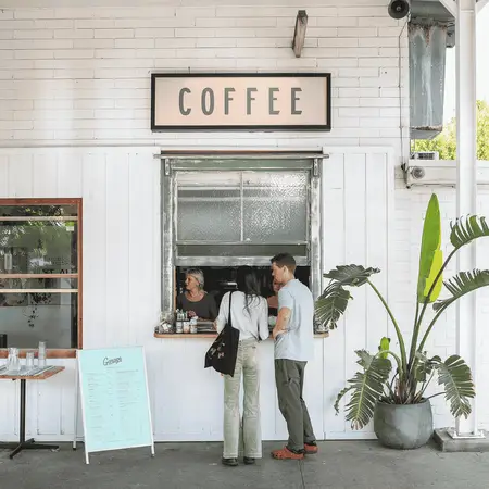 Two people standing at a hole in the wall cafe, ordering coffee