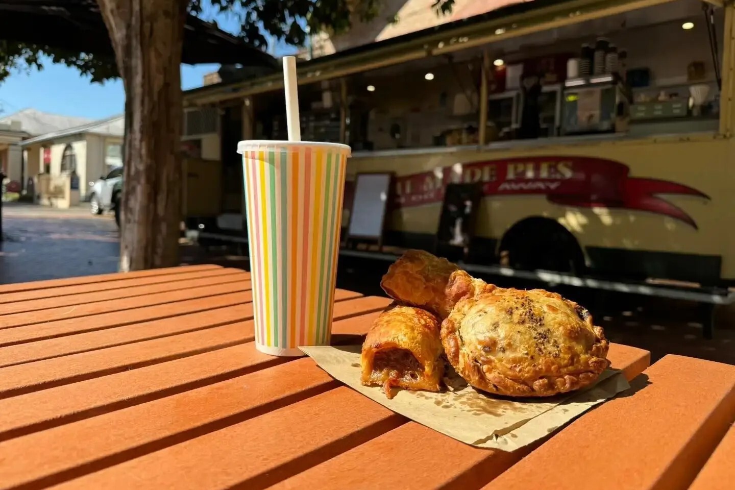 Meat pies and a drink on an outdoor table at the Lismore Pie Cart.