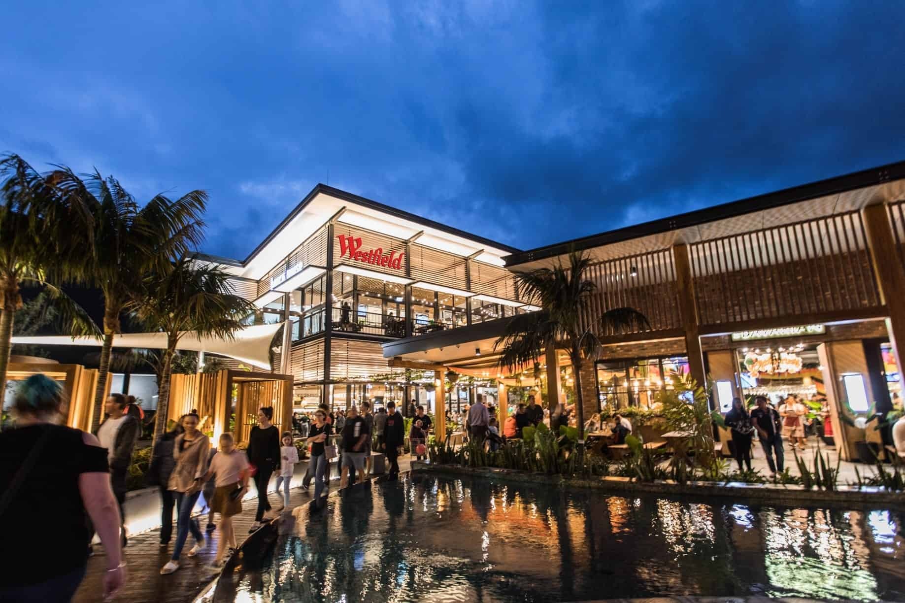 Shoppers outside Westfield Coomera Town Centre beside a pond.