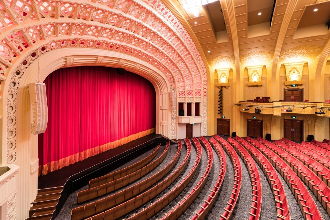 Interior of the Empire Theatre featuring red seating, a curtained stage and ornate arches.