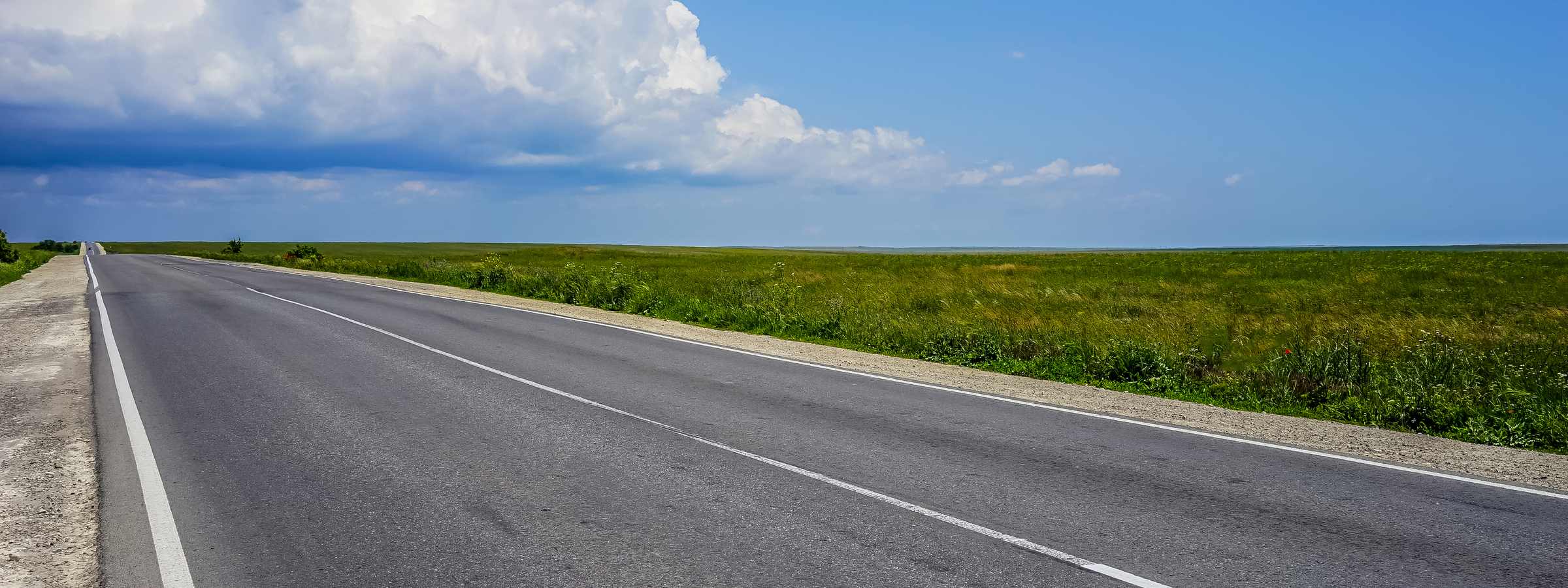 A long highway with no cars on the overgrown grass of the steppe under a blue cloudy sky